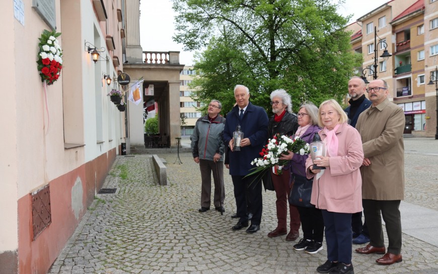 Znicze i kwiaty przed tablicą upamiętniającą Jerzego Szmajdzińskiego