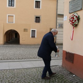 Znicze i kwiaty przed tablicą upamiętniającą Jerzego Szmajdzińskiego