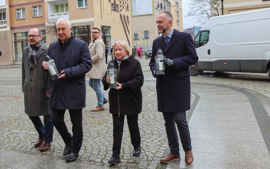 Znicze i kwiaty przed tablicą upamiętniającą Jerzego Szmajdzińskiego