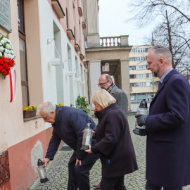 powiększ zdjęcie: Znicze i kwiaty przed tablicą upamiętniającą Jerzego Szmajdzińskiego
