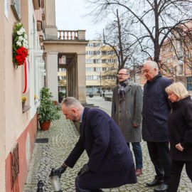 powiększ zdjęcie: Znicze i kwiaty przed tablicą upamiętniającą Jerzego Szmajdzińskiego