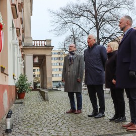 powiększ zdjęcie: Znicze i kwiaty przed tablicą upamiętniającą Jerzego Szmajdzińskiego