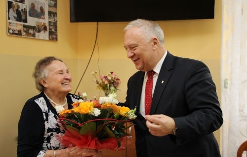 na zdjęciu widać prezydenta tadeusza krzakowskiego, który wręcza kwiaty starszej pani